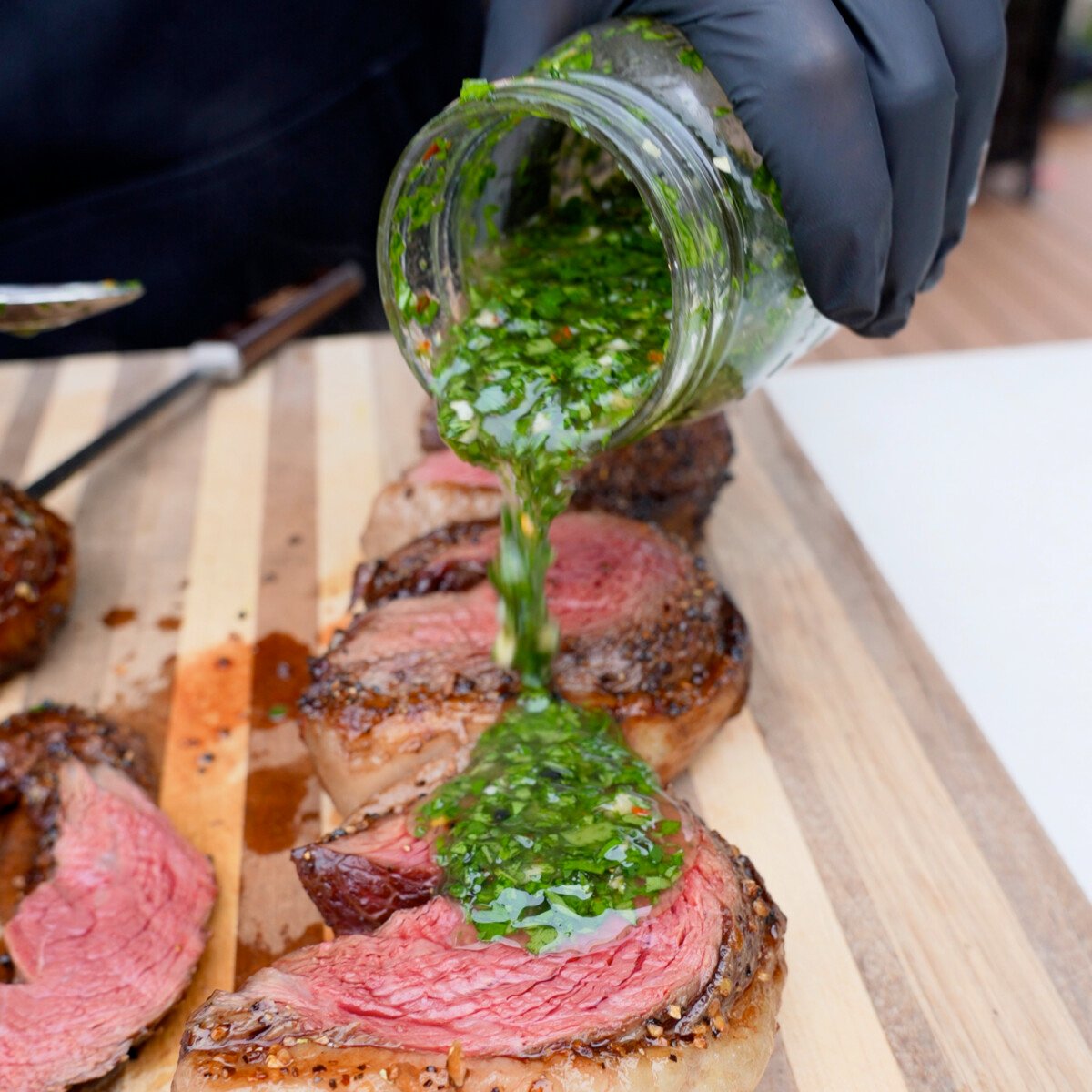 Pouring smoked chimichurri sauce over grilled steak.