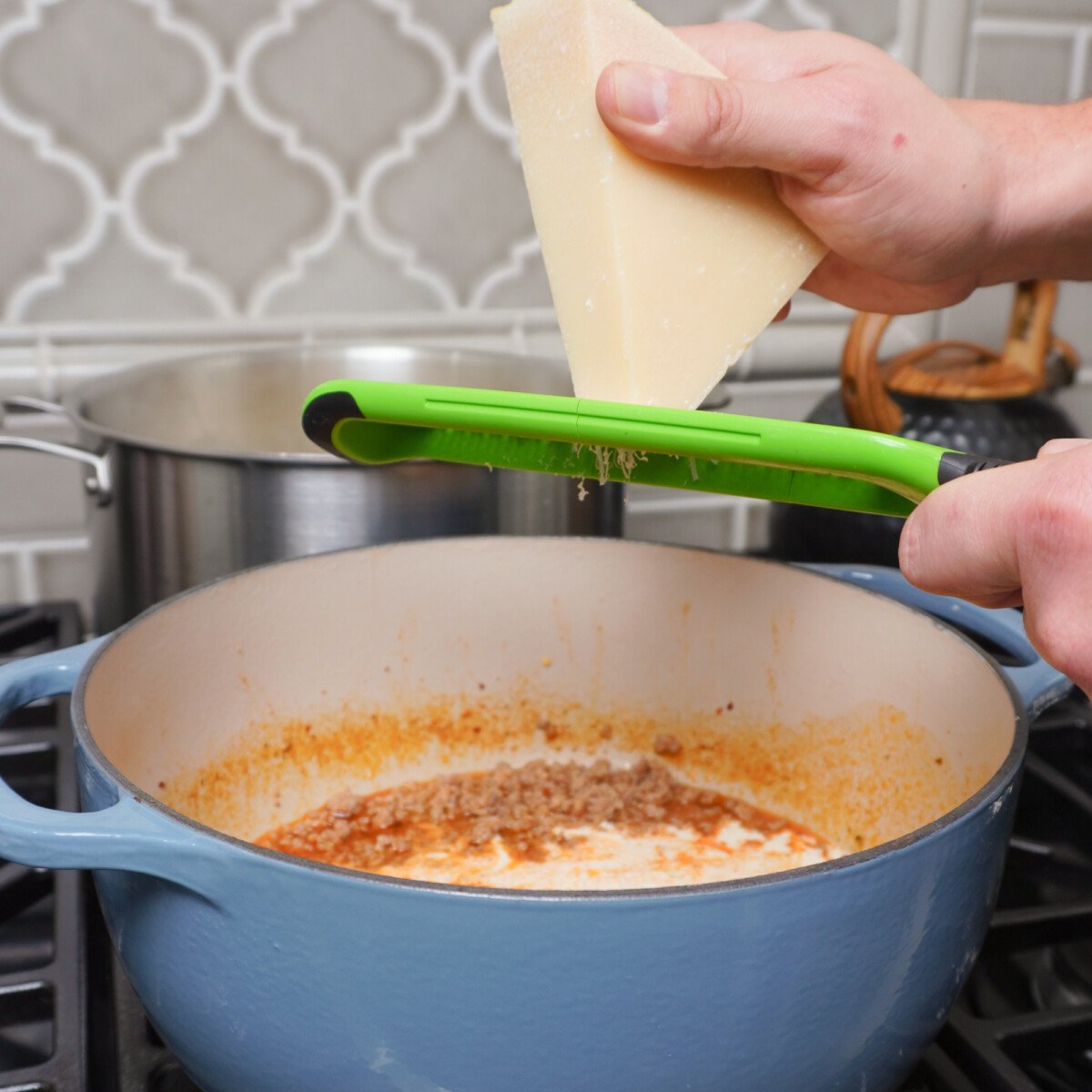 Grating a parmesan wedge over a pasta filled blue dutch oven.