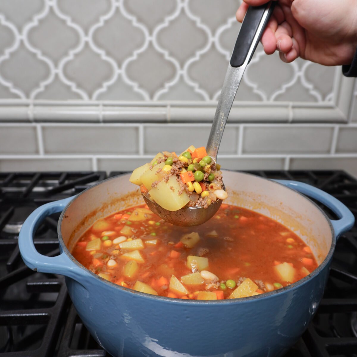 a heaping scoop of the hearty cowboy soup over blue dutch oven on stove top.