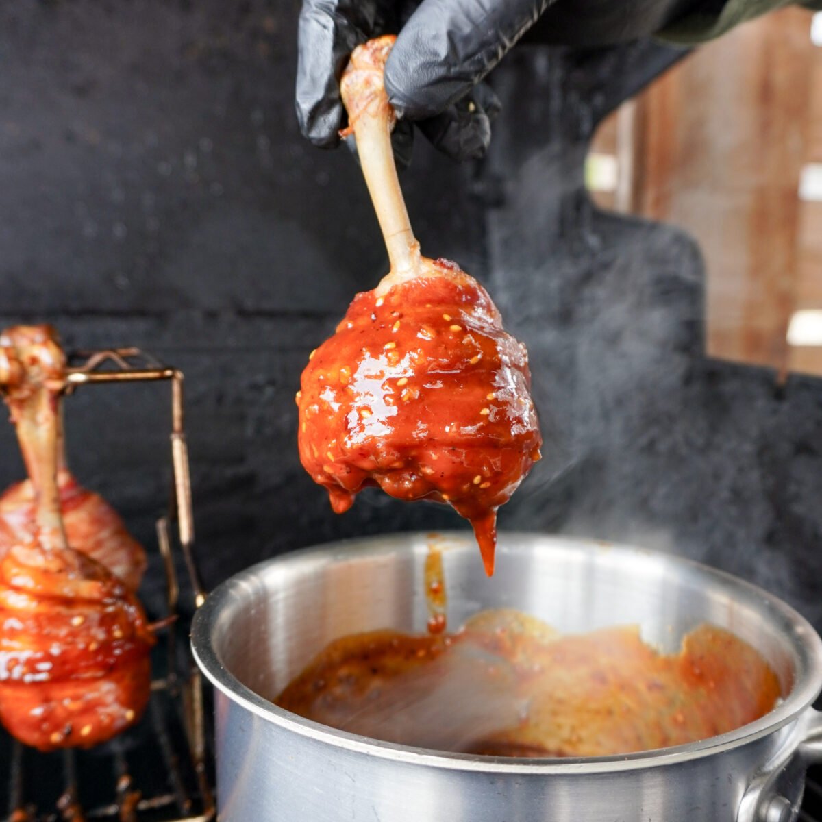 Dunking the bacon wrapped chicken drumsticks in a chili crunch honey BBQ sauce.