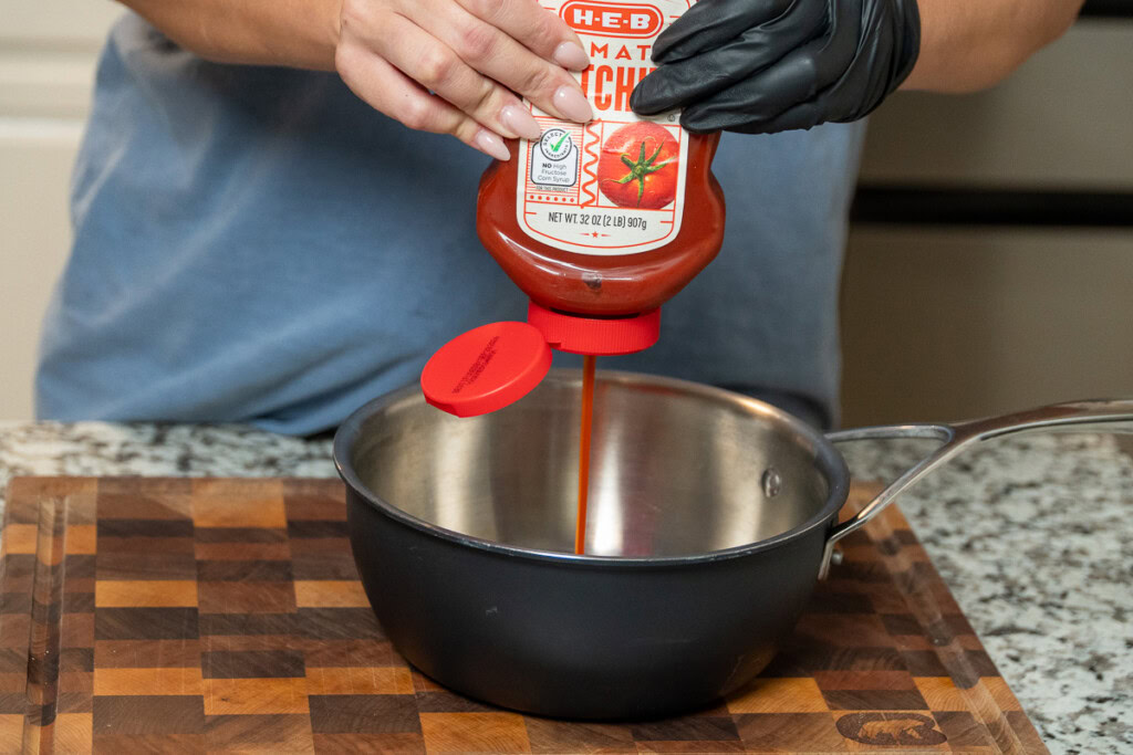 two hands squeezing ketchup in a metal bowl