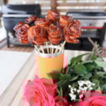 Grilled Bacon Roses in a Yeti Tumbler next to fresh pink roses.