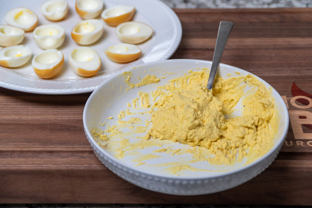 smoked deviled egg filling in a white bowl with a fork