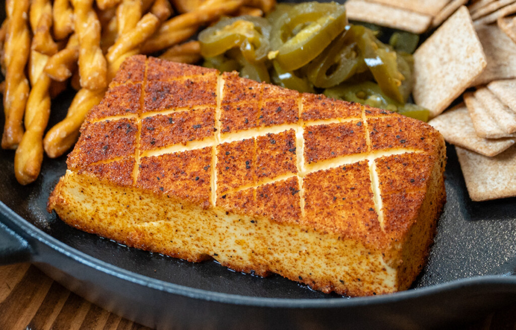 Smoked cream cheese with a seasoned crust, scored in a crosshatch pattern, served in a cast iron skillet with pretzels, crackers, and pickled jalapeños. A perfect smoky appetizer for BBQ gatherings.