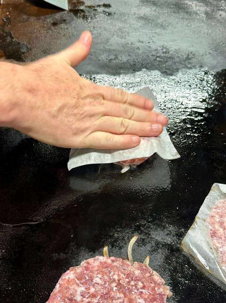 Placing four ounces of ground pork on top of the sliced onion on a griddle grill.