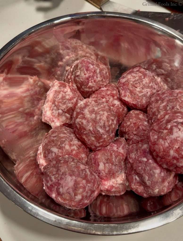 4 ounce portions of ground pork rolled into balls in a stainless steel bowl
