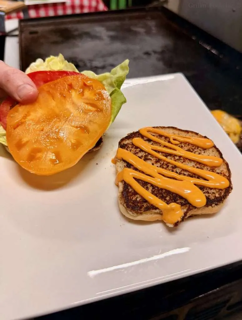 Sriracha mayo on one toasted bun and lettuce and both yellow and red tomato on another toasted bun