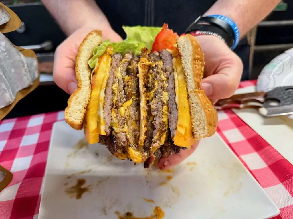 A triple decker, ground pork smash burger cut down the middle. The burger is displayed of a cross section both halves, glistening with juices and gooey cheese.