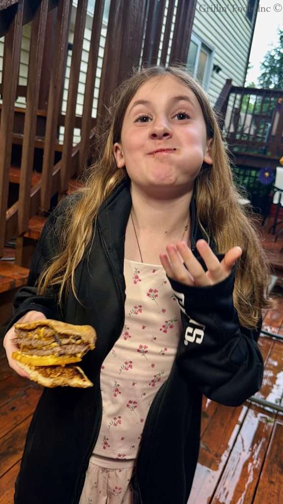 Pretty 10 year old girl eating a triple decker, ground pork smash burger.