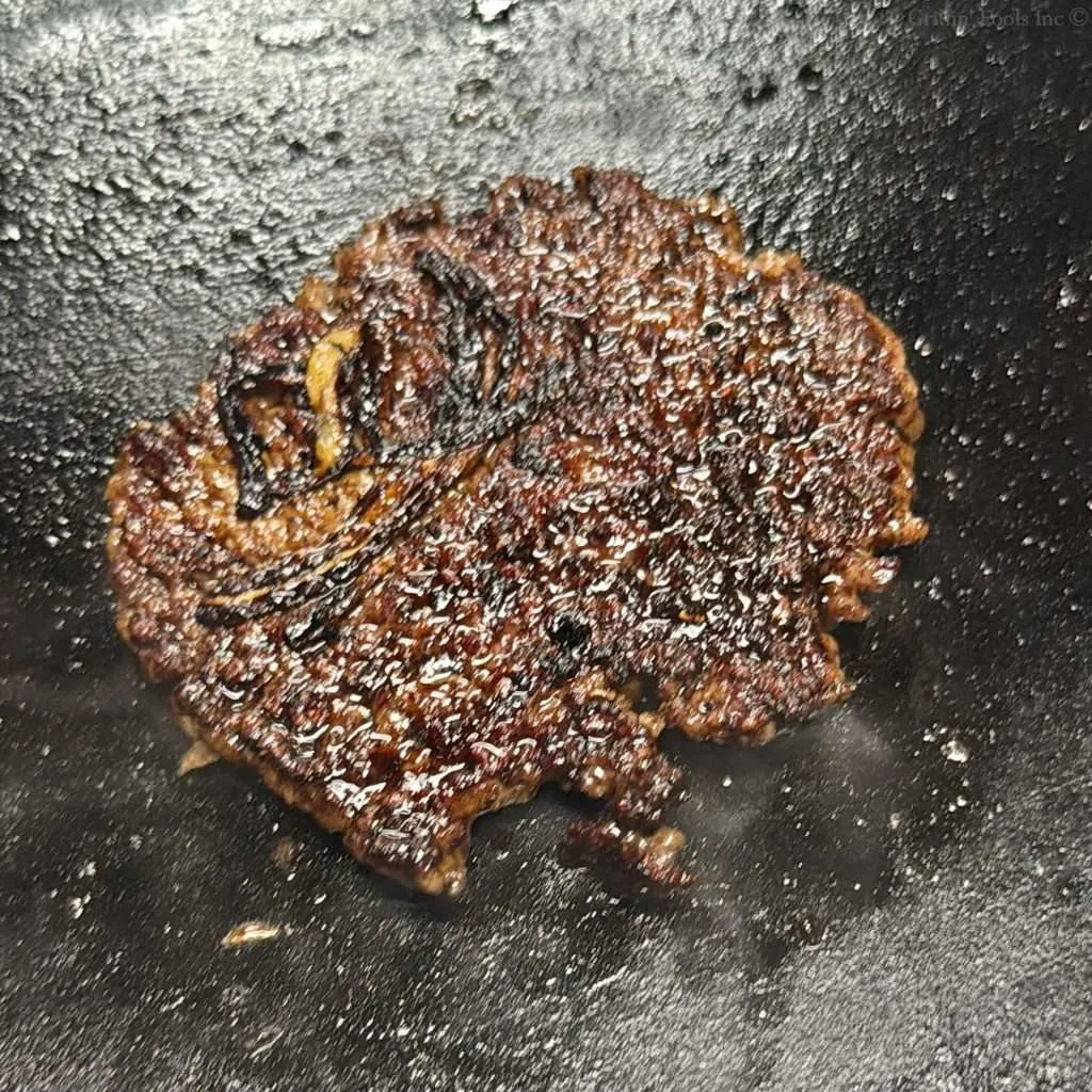 Perfectly browned ground pork burger patty with the crispy edges on a cast iron griddle