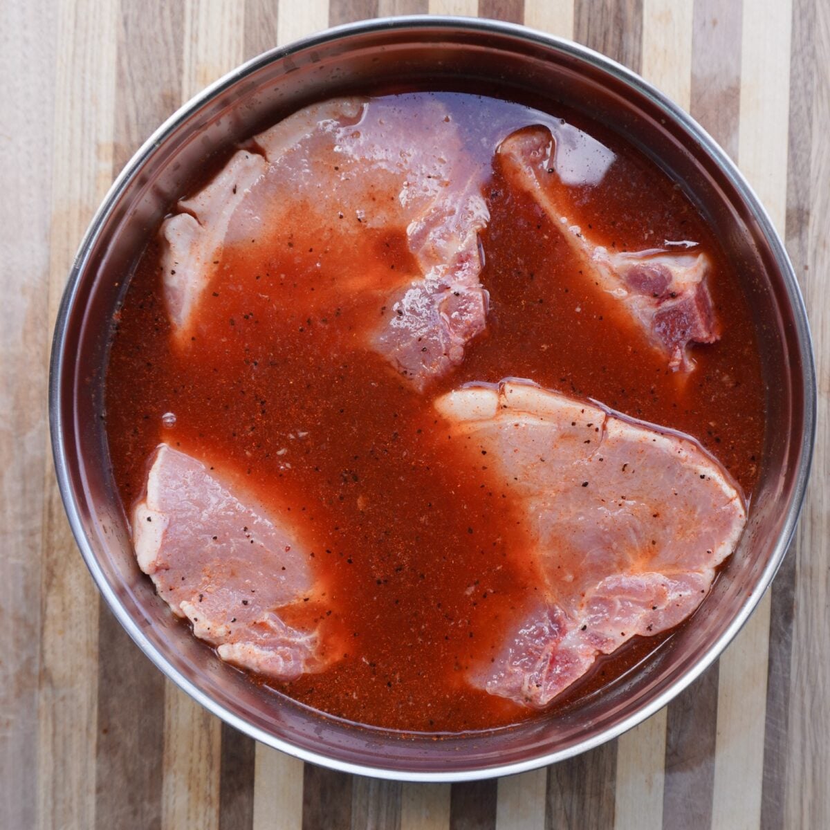 apple juice and cider vinegar brine with raw pork chops marinating inside bowl.