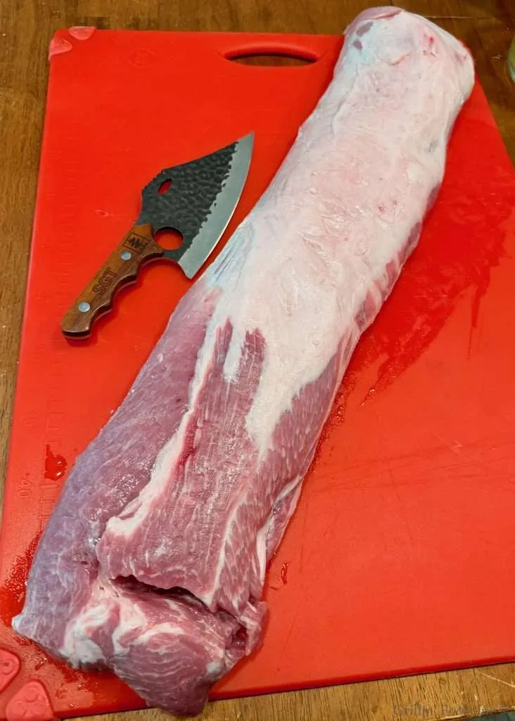 A whole pork loin on a red cutting board with a wicked looking knife