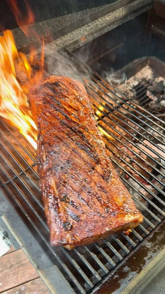 Smoked pork loin searing on a charcoal grill with flames and smoke nearby, glaze caramelized.