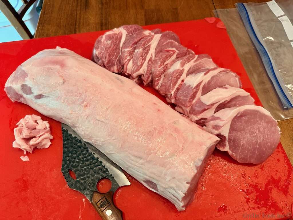 Raw pork loin on a red cutting board with sliced pork chops and a small pile of minced meat nearby; a knife rests on the board with a plastic bag in the background.