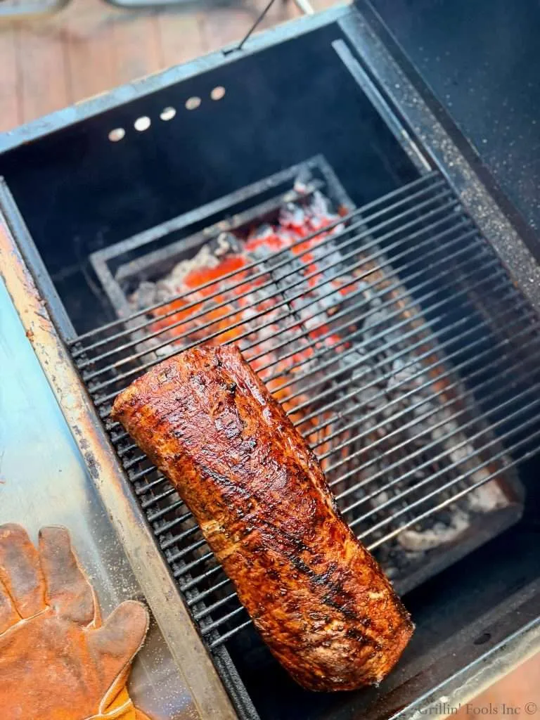 Thick piece of barbecued meat with a caramelized glaze on a grill over hot charcoal.
