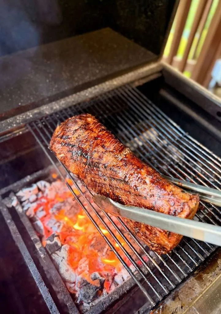 Barbecued pork roast being grilled over hot charcoal with a pair of tongs gripping it