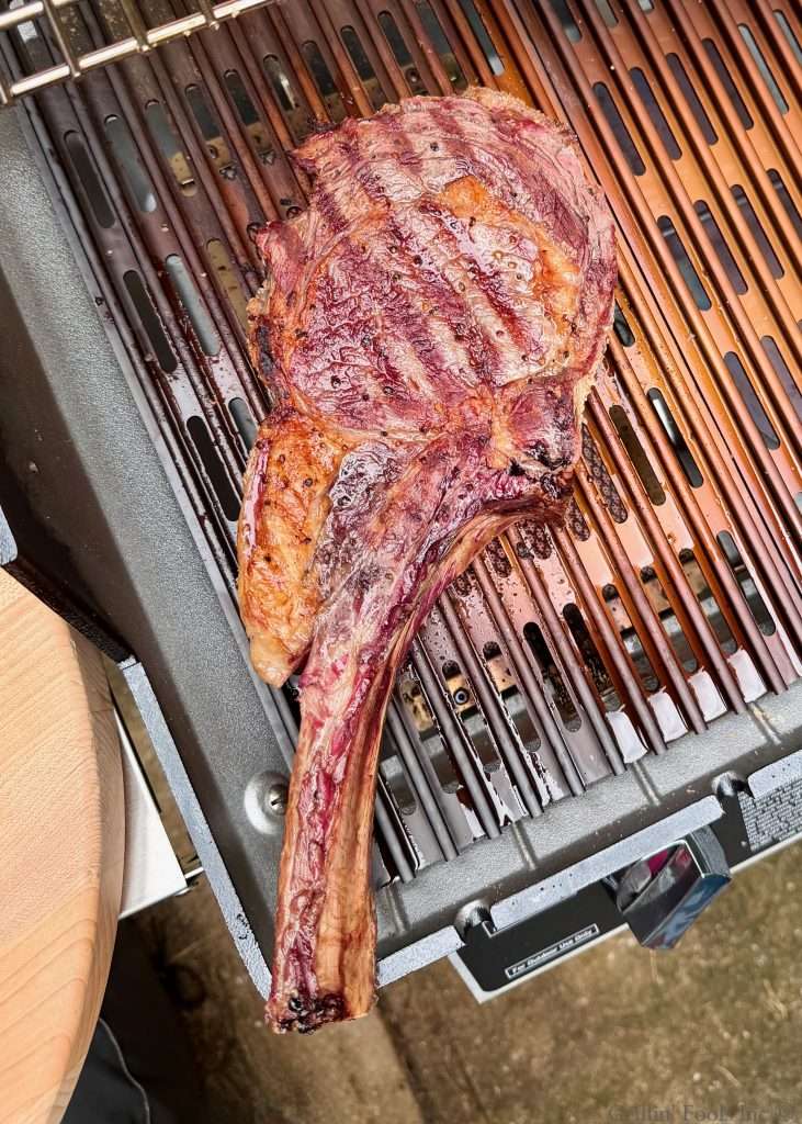 A charred tomahawk steak over the top of a sear station on an MHP Hybrid grill