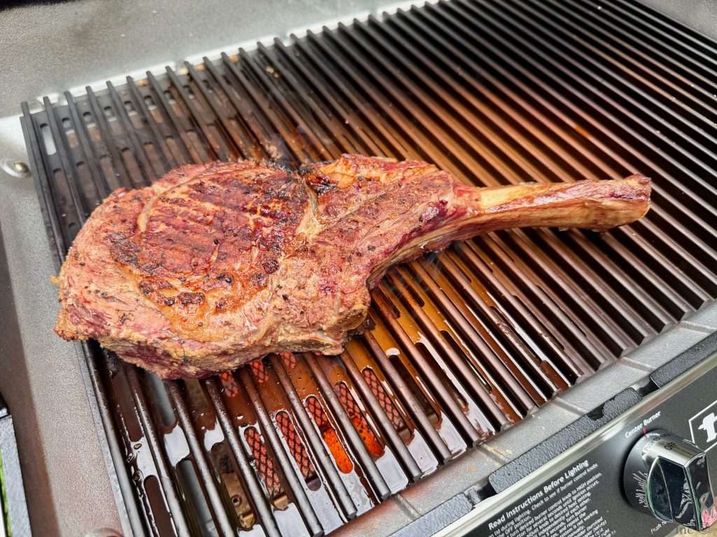 A charred tomahawk steak over the top of a sear station on an MHP Hybrid grill