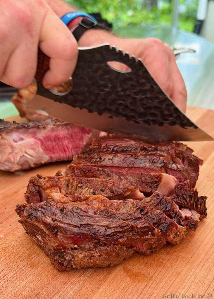 Carving a tomahawk steak on a cutting board with a wicket looking knife