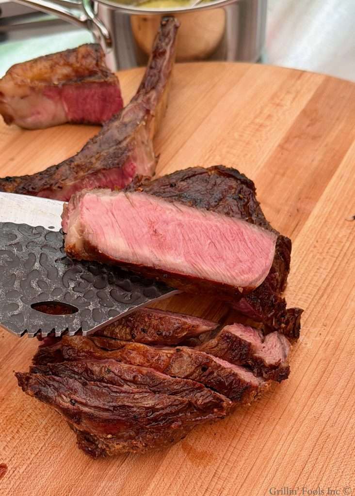 A tomahawk steak carved into slices with one slice being displayed to see the pink, medium rare interior of the steak