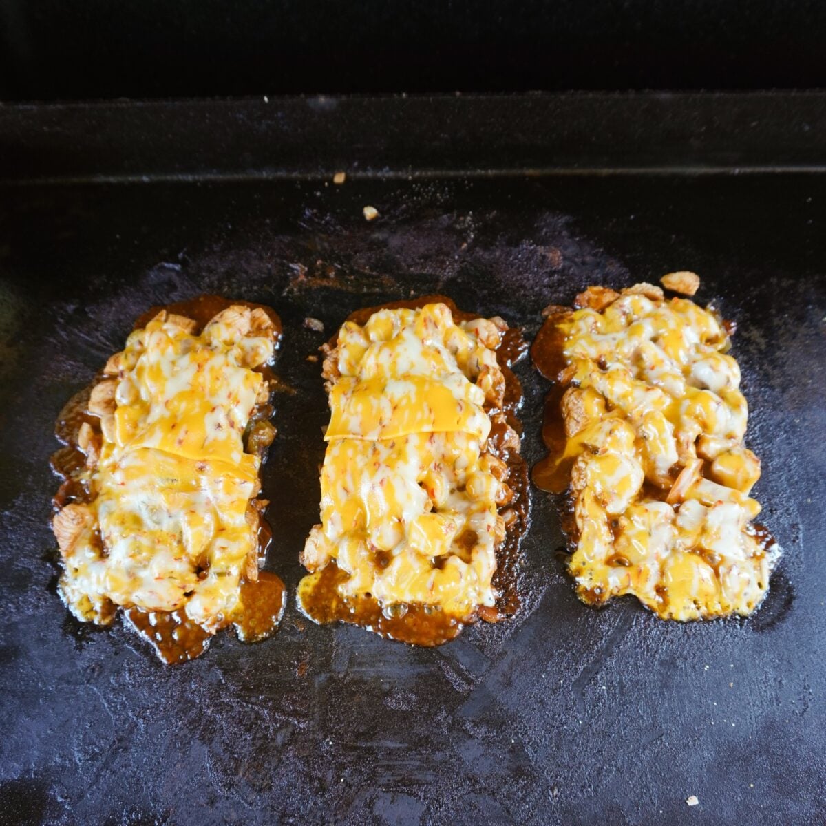 individual servings of grilled chicken with melted cheese on griddle surface.