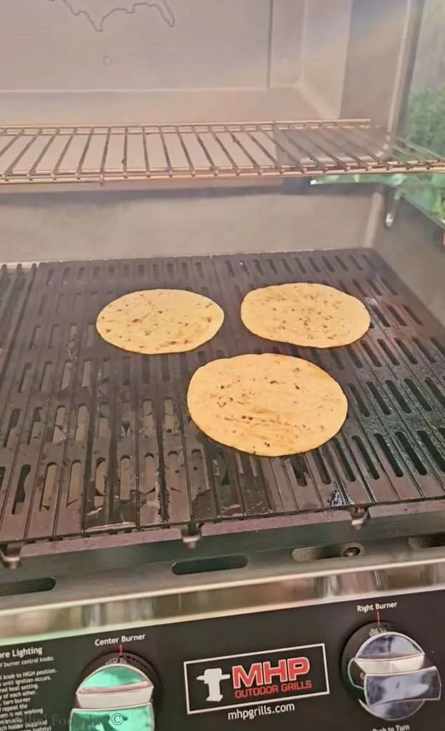Three tortillas cooking on a grill pan inside an outdoor gas grill.