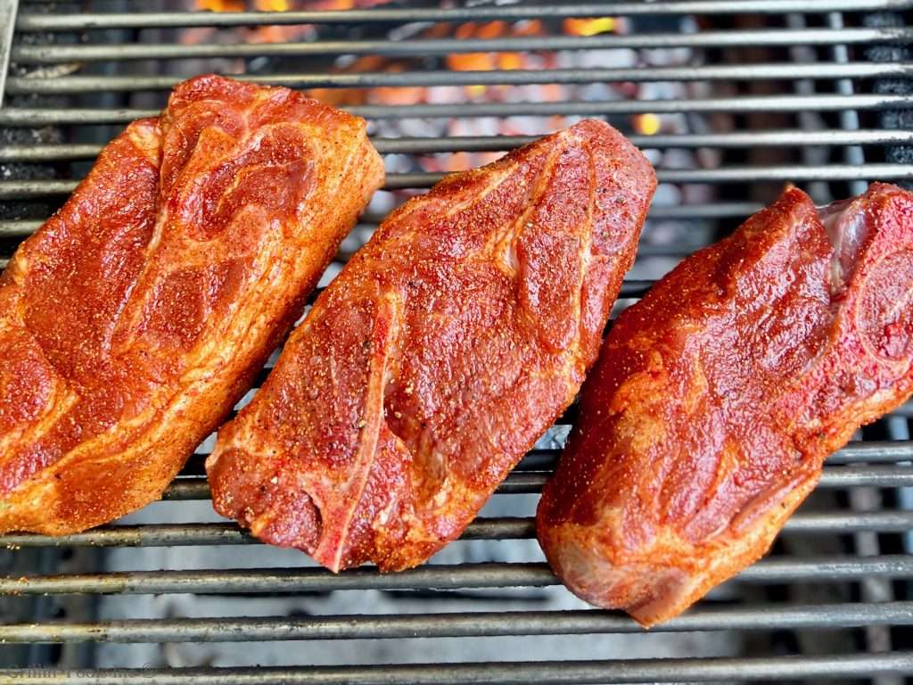 Three raw, seasoned pork steaks resting on top of grill grates as viewed from directly above in the ultimate guide to pork steak