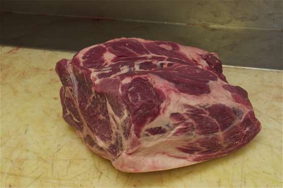 A pork shoulder sitting on the white counter/cutting board in a butcher shop