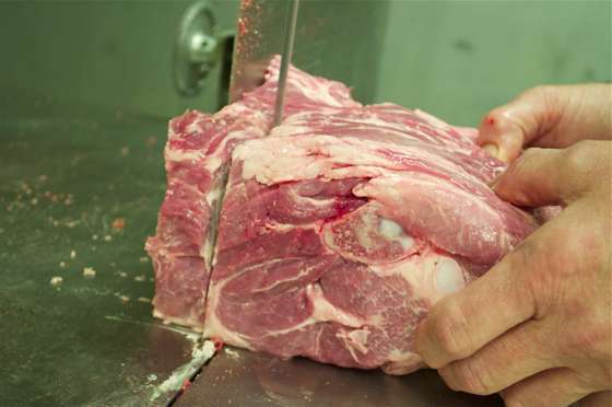 A pork shoulder being run through a band saw to carve off inch thick pork steaks