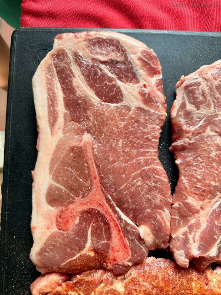 A single pork steak, with lots of veins of fat on a black cutting board. A single pork steak, with lots of veins of fat on a black cutting board.