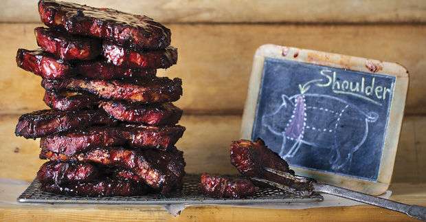 A pile of pork steaks, stacked high next to small chalkboard with a diagram of a pig in chalk