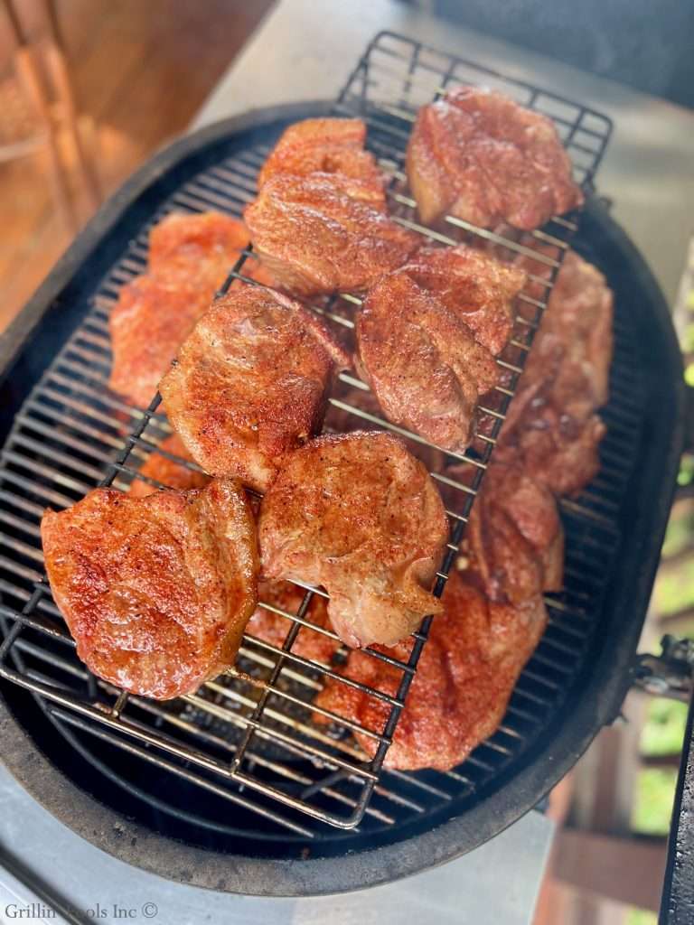 Raw, seasoned, half pork steaks on a wire rack over a round barbecue grill.