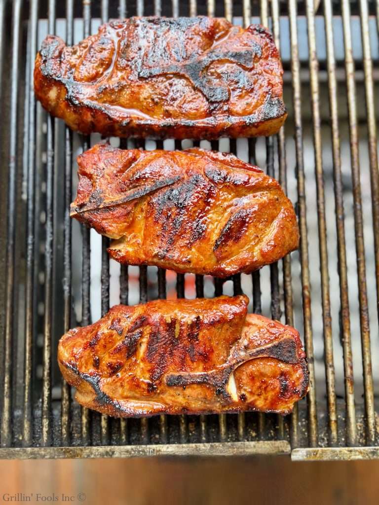 Grilled pork steaks with charred edges cooking on a barbecue grill over hot grates.