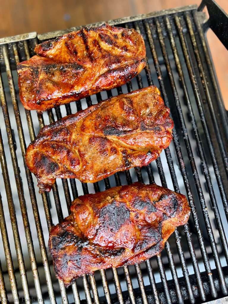 Pork shoulder steaks grilling on a hot barbecue with a caramelized glaze and charred edges.