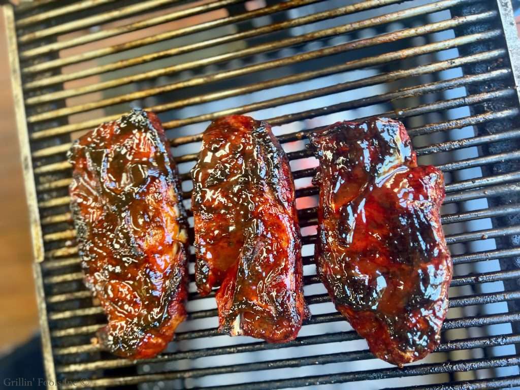 Sauced pork steaks cooking on a hot barbecue grill with a charred glaze.