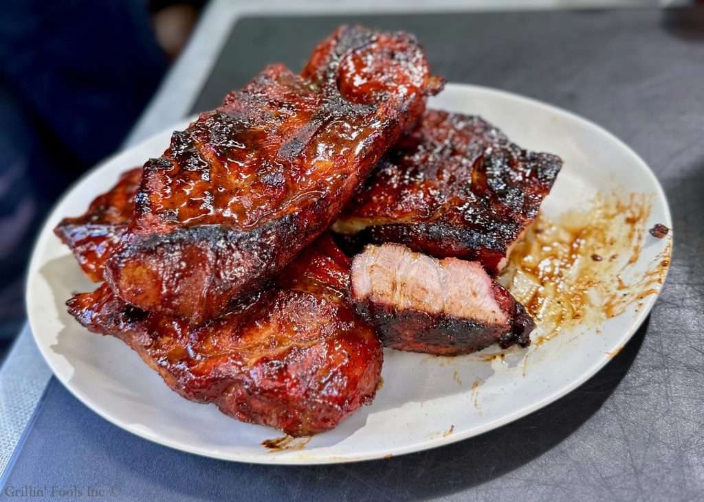 Glazed barbecue pork steaks piled on a white plate with a sticky, caramelized crust and sauce stains nearby