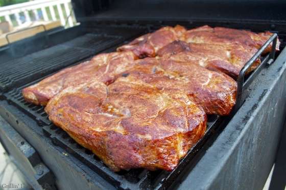 Multiple seasoned pork steaks turning a glorious golden red color on a barbecue grill
