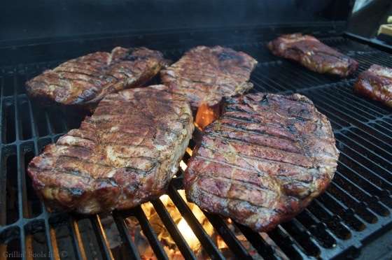 Grilled pork steaks searing on a barbecue grill with flames beneath the grate.