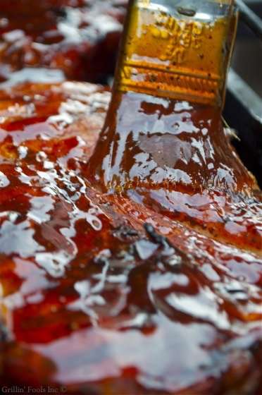 Close-up of a brush spreading glossy red barbecue sauce over a reverse sear pork steak