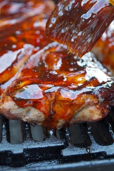 Barbecued pork steak with a glossy barbecue sauce cooking on a grill over metal grates.