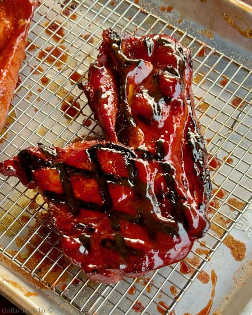 Cooked, glazed red pork steak resting on a cooling rack with sauce drippings around it