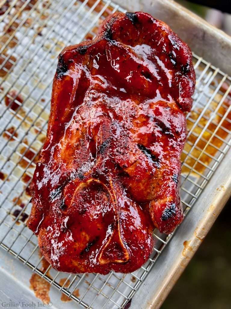 Glazed barbecued pork steak with red-brown sauce and charred edges on a metal rack.