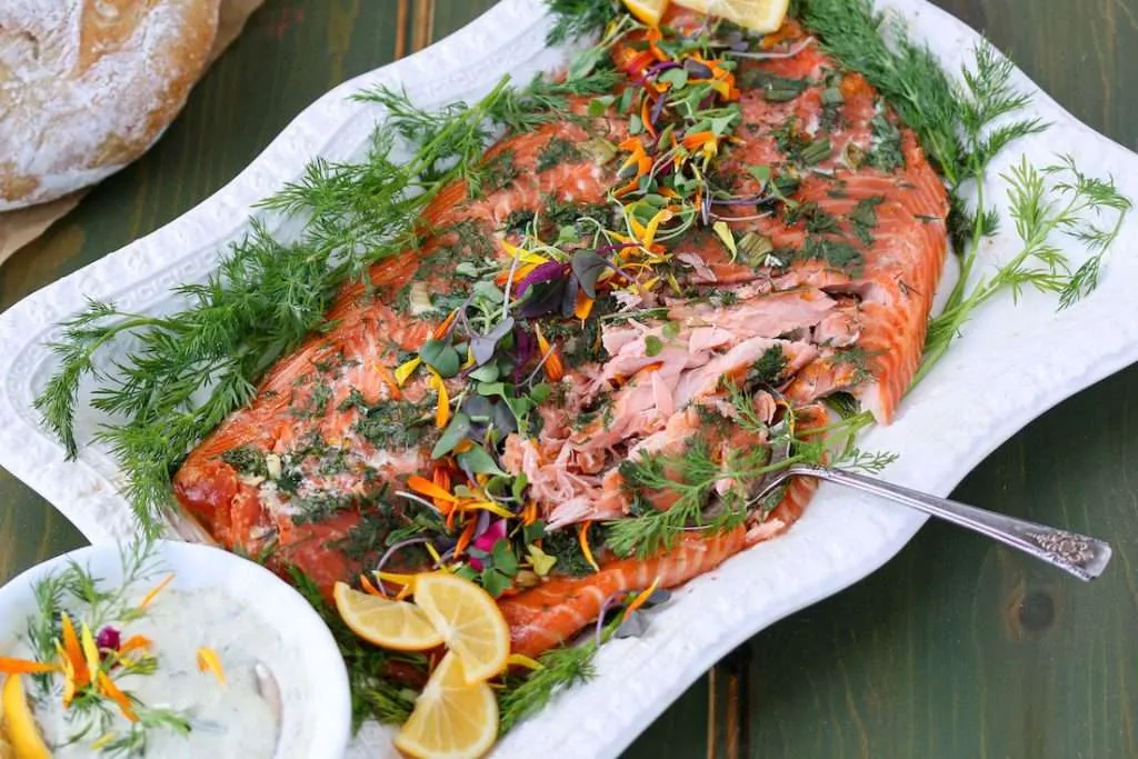 Lemon and Dill Smoked salmon on a platter, next to a bowl of creamy dill sauce, garnished with fresh dill and lemon slices