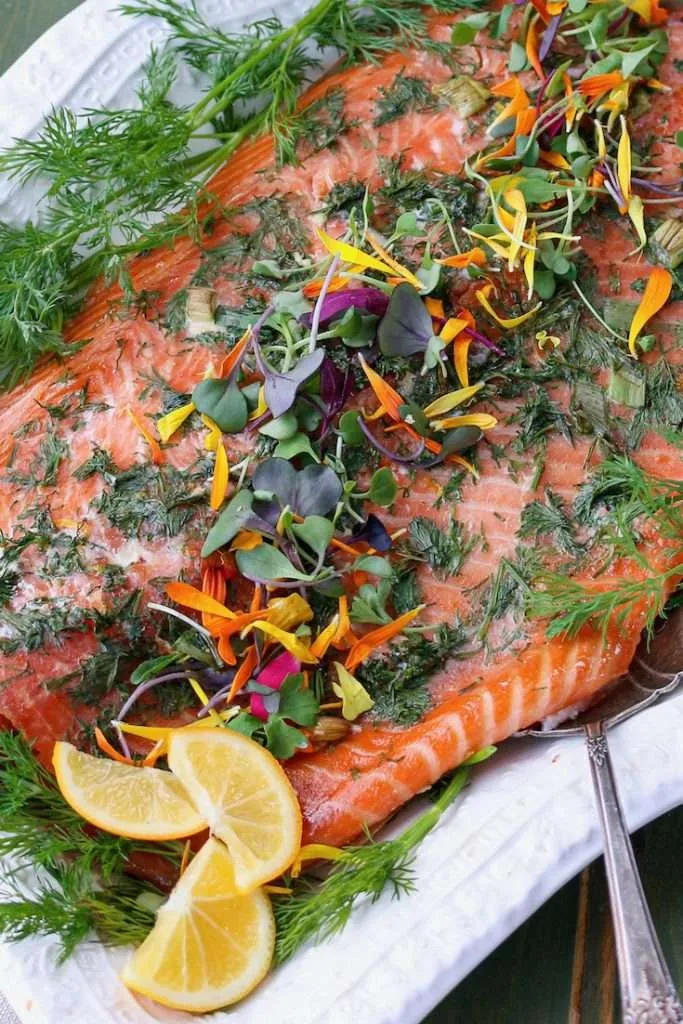 Salmon fillet garnished with dill, herbs, edible flowers, and orange slices on a white platter