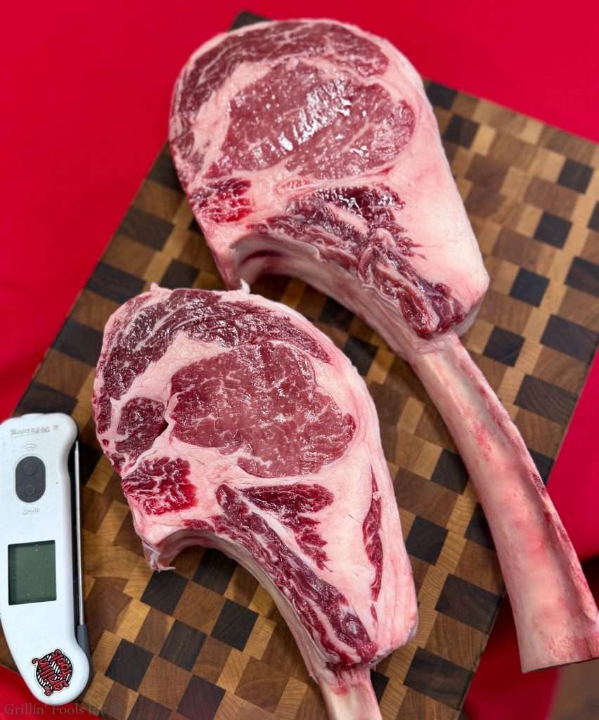 Raw beef ribeye on a wooden cutting board with a white digital thermometer nearby and a red background behind.