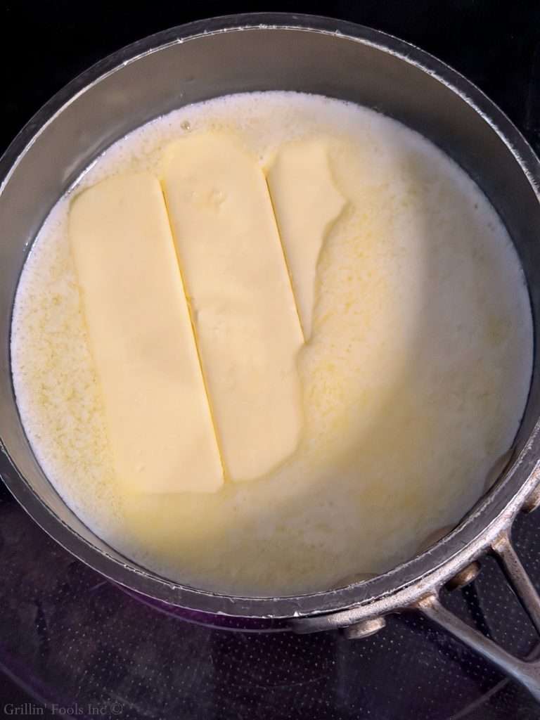 Butter blocks melting in a saucepan on a stove, surrounded by warm melted butter or cream variant liquid.