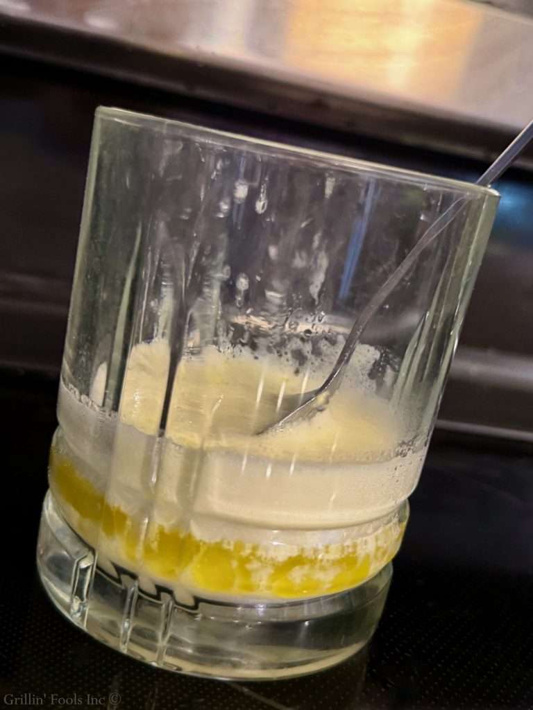 Close-up of a glass with the solids on top of some clarified butter