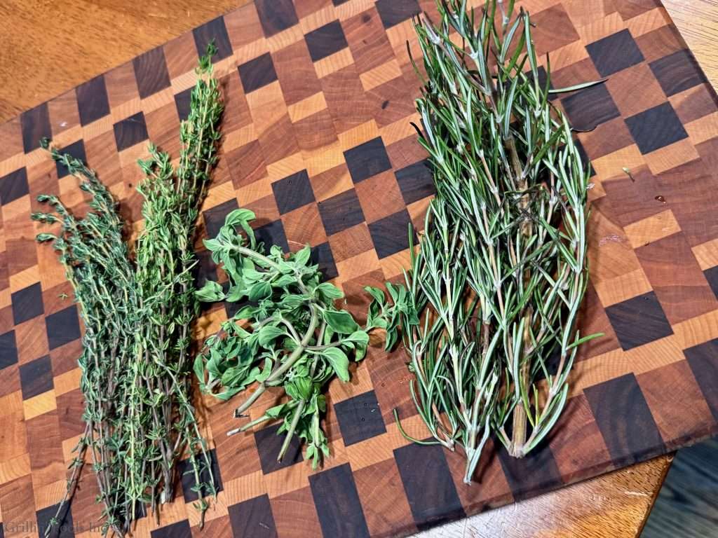 Bundles of fresh herbs (thyme, oregano, and rosemary) on a wooden cutting board with a checkered pattern