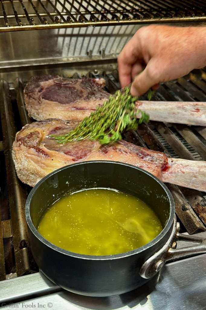 Beef ribeye being brushed with clarified butter from a fresh herb mop