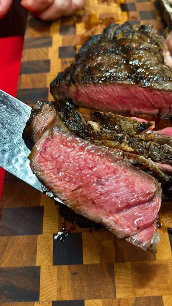 Sliced medium-rare beef steak with a dark seared crust on a wooden cutting board.